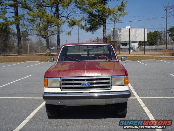 Red and white Ford F-250 truck, front view, faded paint, parked in lot