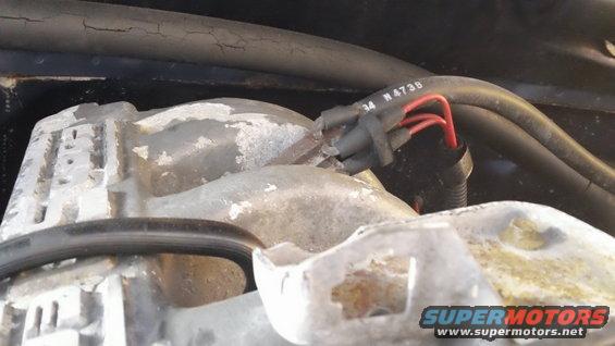 Close-up of a gray engine component with red-tipped wires connected to a black connector. Text '34 N473B' is visible on a black hose
