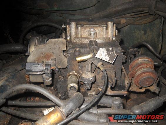 Close-up of a dirty engine carburetor with electrical connectors and hoses attached