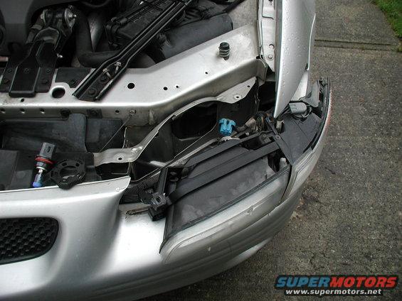 Silver car's front headlight assembly removed, showing engine bay components