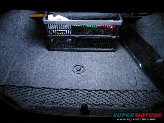 Car trunk with a black plastic basket holding items, including an umbrella and colorful containers. A cargo net is at the bottom