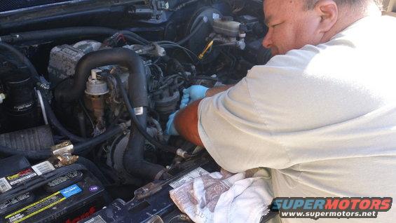 man in blue gloves working on engine bay, battery visible