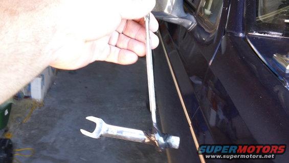 Hand holding a wrench near the side of a dark blue vehicle