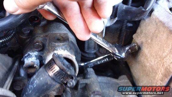 Close-up of engine component with a hose clamp and a wrench being used