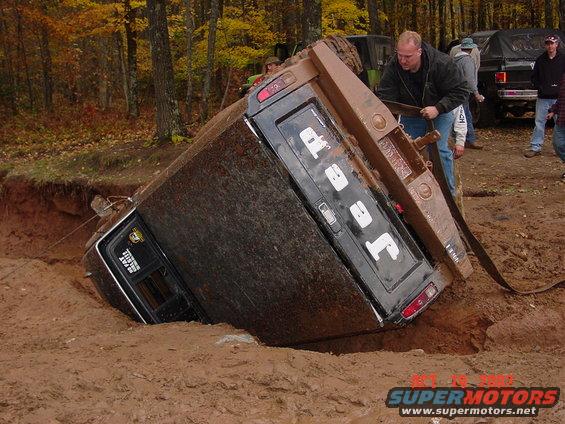 Jeep J-10 truck tipped over in a muddy hole with people trying to pull it out