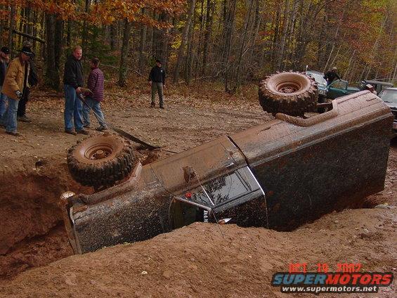 Overturned 1986 Jeep J-10 in mud pit with spare tire on roof