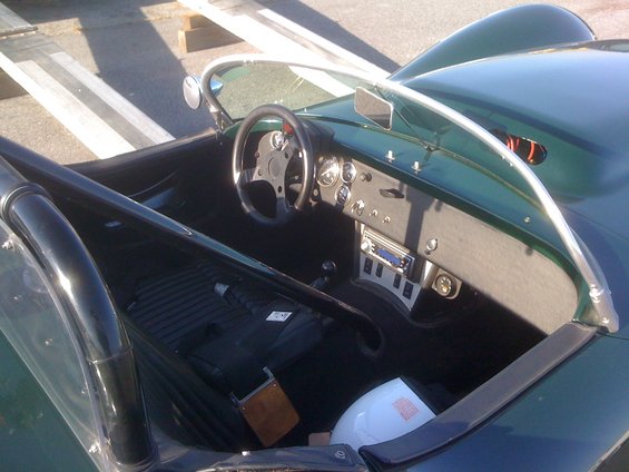 Interior view of a green vintage sports car, showing dashboard, steering wheel, roll bar, and seats