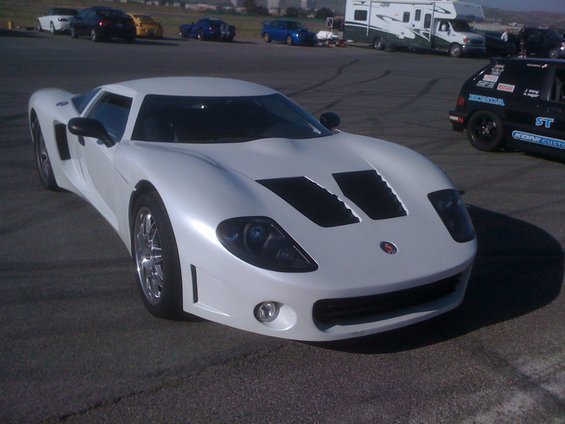 White sports car with black hood vents and headlights, parked on asphalt