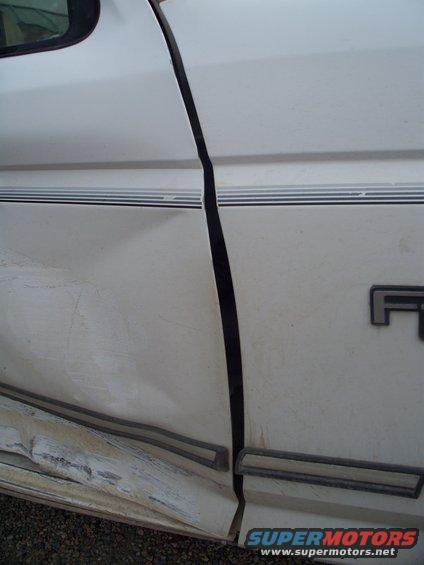 Side view of a damaged white 1992 Ford F-250 door with trim and dented lower panel