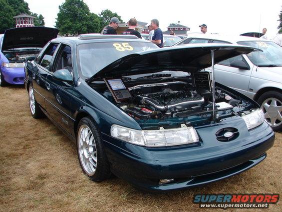 Dark green sedan with hood open, showing engine and a laptop. Number 85 on windshield