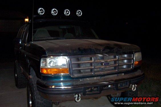 Dark green Ford Bronco front view with four lights on roof rack. Grille is chrome
