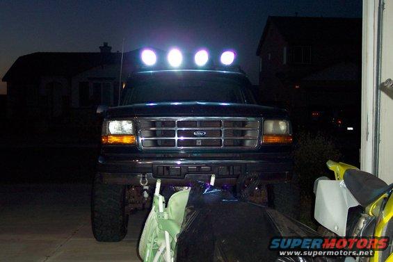 Front view of a 1995 Ford Bronco with a light bar on top, parked in a driveway at dusk
