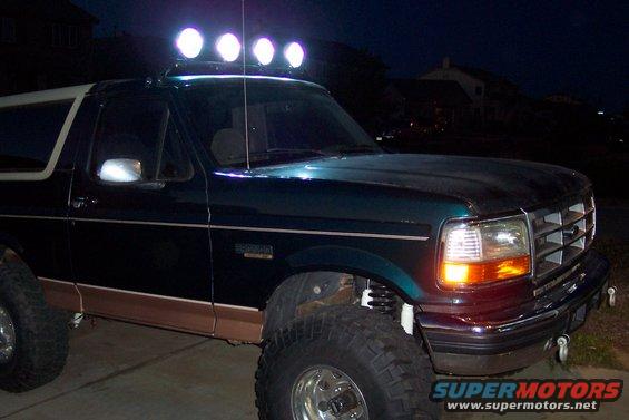 Dark green Ford Bronco with tan trim and a light bar on the roof, viewed from the front 3/4 angle