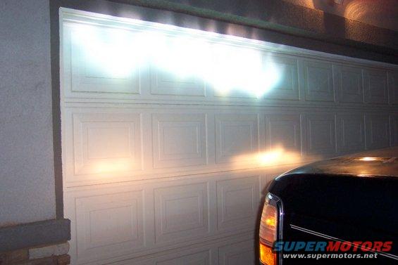 Headlights illuminate a garage door; part of a dark vehicle visible