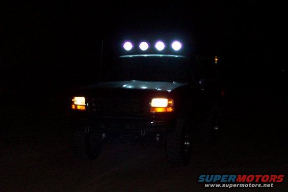 Front view of a dark-colored truck at night with four lights on the roof rack illuminated