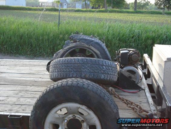 Trailer bed with three tires, one damaged, and a winch. Wooden planks form the bed