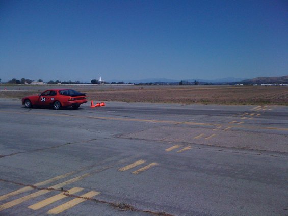 Red sports car with number 34 on the door, parked on a racetrack with orange cones