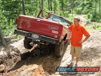 Red Ford pickup truck stuck on a muddy trail with a man standing next to it