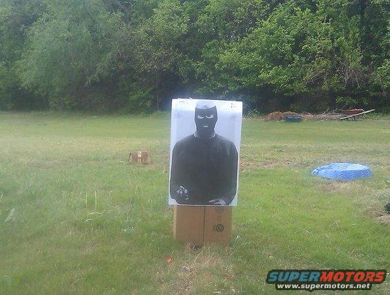 Target of a person wearing a balaclava, standing on cardboard boxes in a grassy field