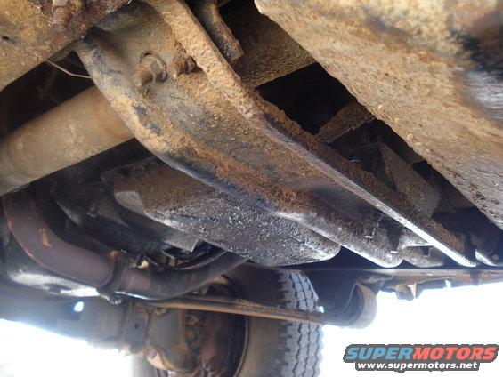 Underside view of rusty truck frame, exhaust pipe, and tire. Supermotors.net logo visible