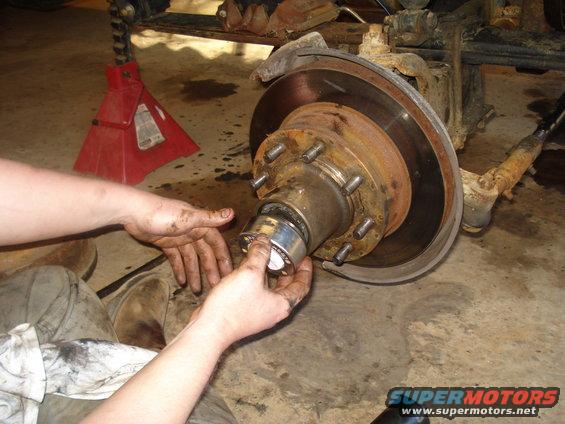 Hands working on a rusty wheel hub assembly with a red jack stand in the background