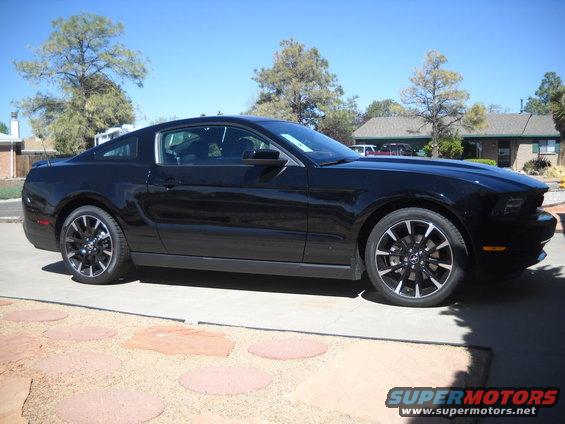 Black coupe parked in a driveway. It has black rims with silver accents