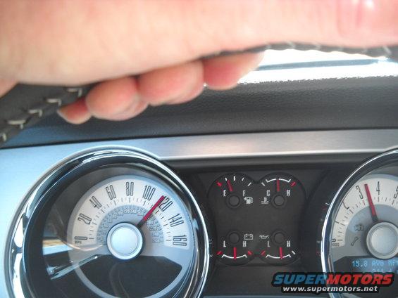 Driver's hand on steering wheel, showing car's speedometer and fuel gauges. Speedometer reads about 115 mph