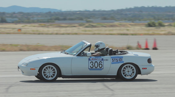 White 1991 Mazda Miata with racing numbers 306 and STS NOV on the side, driven by a person in a helmet on a race track