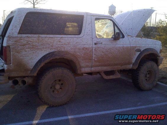 White SUV covered in mud, hood up, parked on pavement