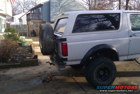 White Ford Bronco rear quarter panel with spare tire on swing away carrier. Visible rear bumper and fender flare