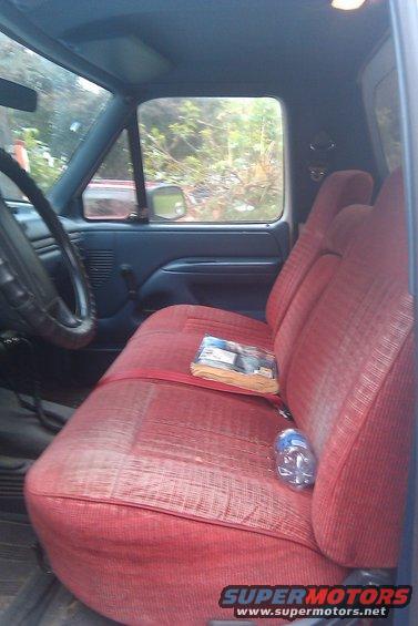 Interior of truck with red bench seat, steering wheel, and window view