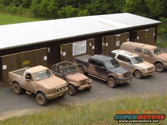 Tan 2004 Ford F-150 pickup truck covered in mud, parked in front of a barn with other vehicles
