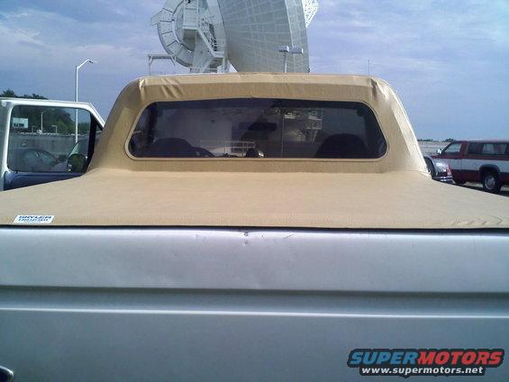 Rear of a silver Ford Bronco with a tan soft top. Another SUV is parked to the right