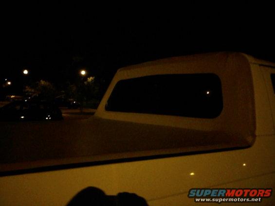 Pickup truck bed with a soft canopy over it. Another car is visible in the background at night