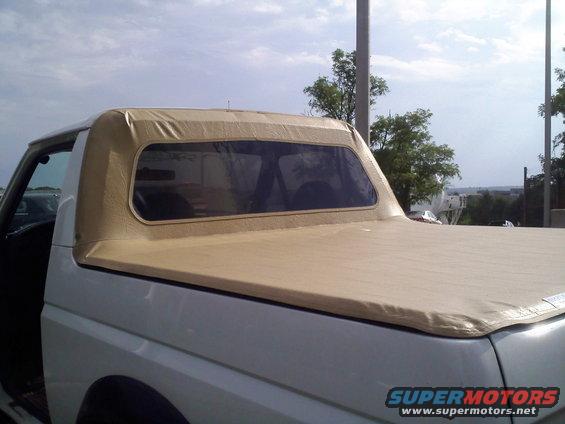 White pickup truck with tan soft top, side view. Visible interior and rear bed cover