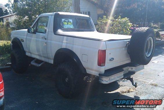 White pickup truck with soft top, spare tire on back, and "FOR SALE" signs in windows