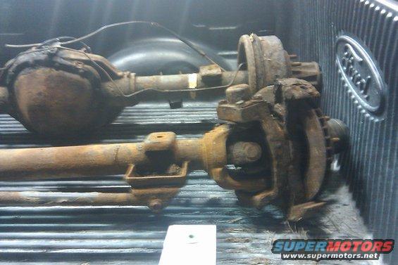 Two rusty rear axles in the bed of a truck, one with a Ford logo visible