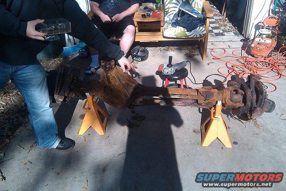 Rusty axle assembly on jack stands with grinder nearby