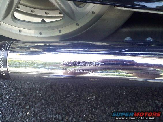 Chrome Rinehart Racing exhaust pipe on a motorcycle, with a silver wheel visible above