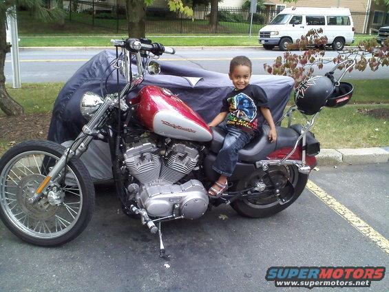 Child sits on a red and silver 2004 Harley-Davidson Sportster Custom motorcycle parked outdoors