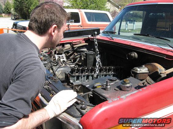 Man working on engine of red 1981 Ford Bronco, another Bronco in background