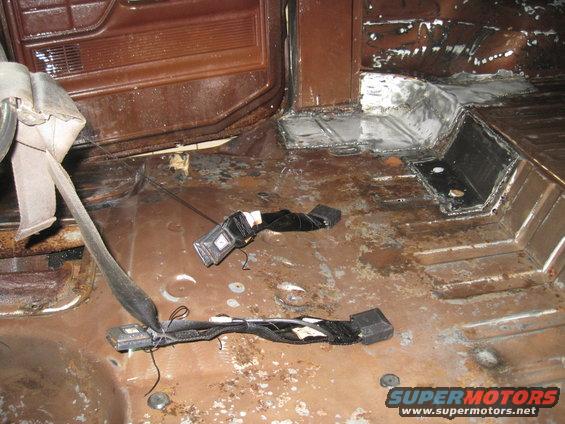 Interior floor of a vehicle with rust and some seatbelt parts on the floor