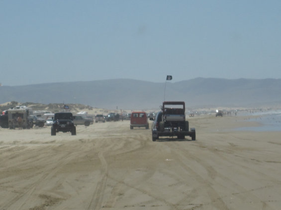 Off-road vehicles driving on a sandy beach with dunes and ocean in the background