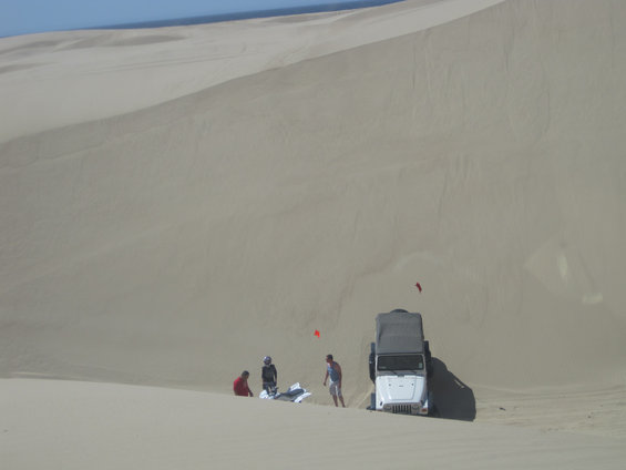 White Jeep Wrangler parked on a sand dune with people nearby