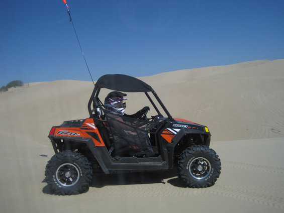 Orange and black side-by-side ATV with rider in helmet on sand dunes
