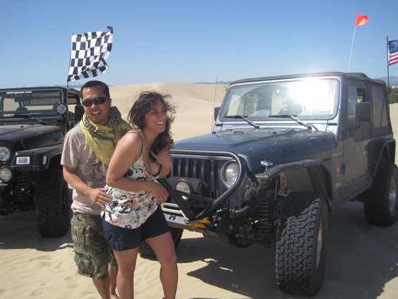 Couple posing in front of two off-road vehicles on sand dunes