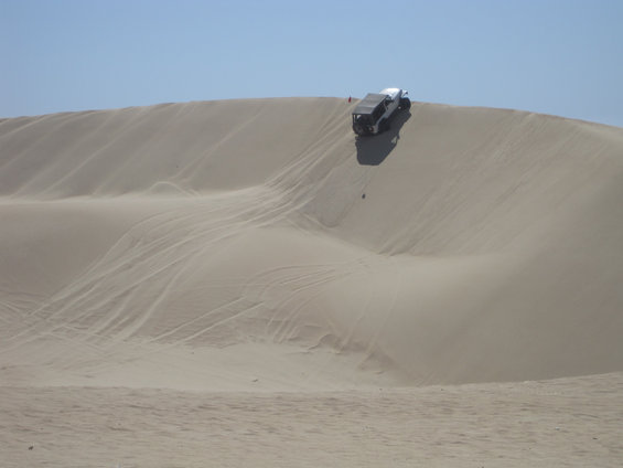 White SUV with black soft top on sand dune, rear view, off-road tires