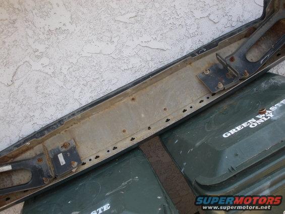 Close-up of a vehicle bumper resting on green trash cans. One can has 'GREEN WASTE ONLY' text