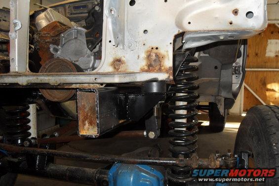 Truck chassis with suspension and engine components visible, showing rust and modifications
