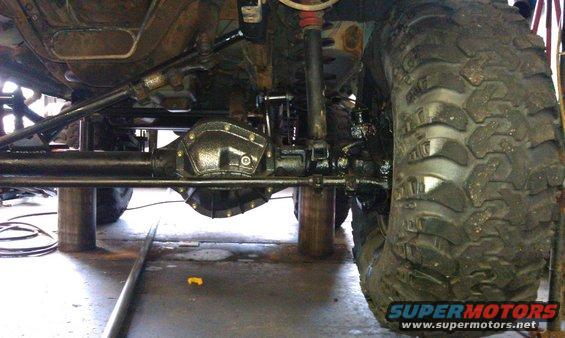 Undercarriage of a lifted vehicle with large off-road tires, showing differential and suspension components